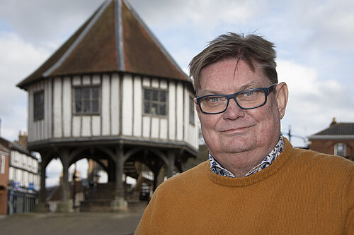 Man in orange top in front of timbered stilted building